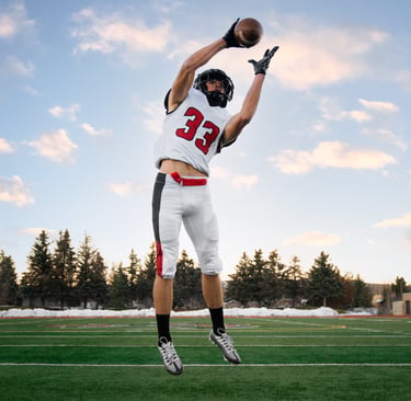 A football player in a white and red jersey jumps to catch a football on a green field.