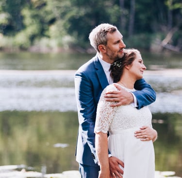 Braut und Bräutigam blicken neben einem See in die Ferne.