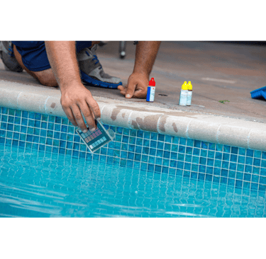 Close-up image of a pool tech kneeling on the edge of a pool performing water testing and balancing