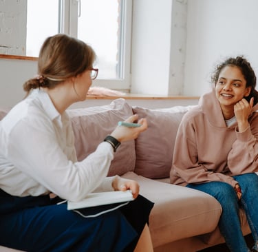 An adolescent girl sitting on a couch smiling and talking to a female therapist