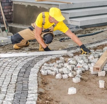 a man in a yellow shirt is laying concrete bricks on the ground