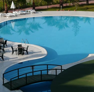 a pool with concrete deck, chairs and tables in a resort