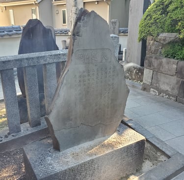 A traditional Japanese stone monument with kanji inscriptions in a Buddhist temple garden.