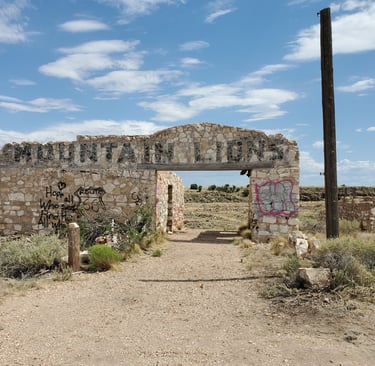 Abandoned stone building ruins with Mountain Lions sign and graffiti at Two Guns on Route 66.