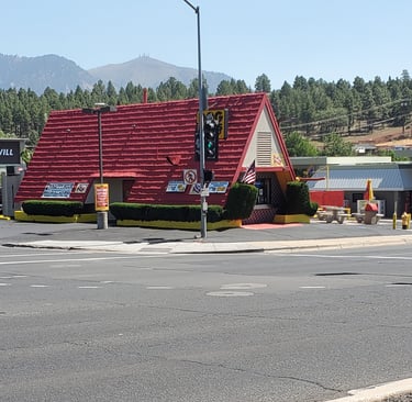 A classic A-frame Wienerschnitzel restaurant with a red roof near a mountain landscape and Goodwill store.
