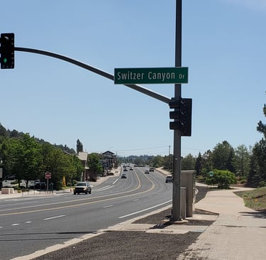 A street sign for Switzer Canyon Drive hanging over a sunny multi-lane highway in Flagstaff Arizona.