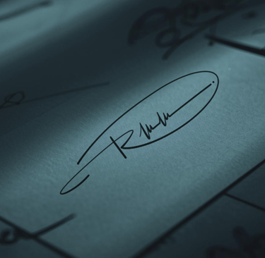 Professional handwritten signature on a business card under moody, dramatic lighting.