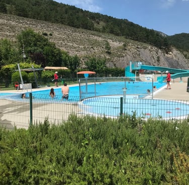 Families enjoy an outdoor swimming pool with water slides at a mountain resort in Axat