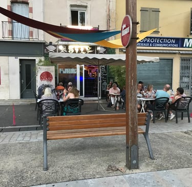 Customers dining at a cozy outdoor restaurant terrace with colorful sun sails. Asily Quillan.
