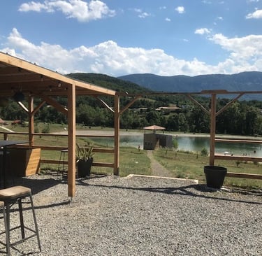 Rustic outdoor patio with wooden pergola overlooking a scenic lake and mountains in Quillan.