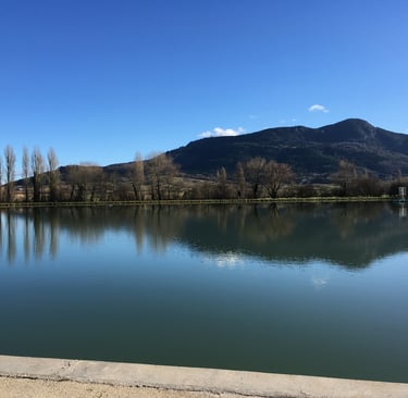 Serene landscape featuring a calm lake reflecting tall trees and a dark mountain  in Puivert.