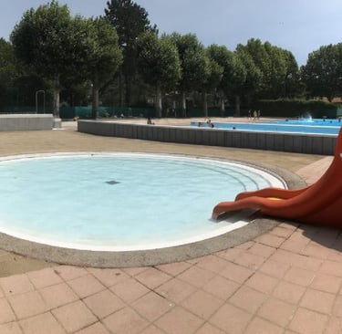 Round outdoor kiddie pool with a red elephant slide at a sunny public swimming Qiullan.