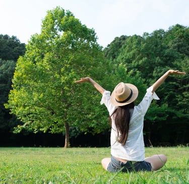 a woman sitting on the grass with her arms outstretched up