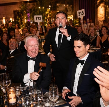 Guests raising bidding paddles during a California fundraising gala while a professional charity auc
