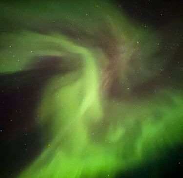 Close-up view of vivid green and purple Northern Lights swirling across a star-filled night sky in the Faroe Islands