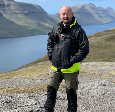 Bogi Olsen, your local Faroe Islands photography guide, standing outdoors with camera gear and scenic fjords behind him