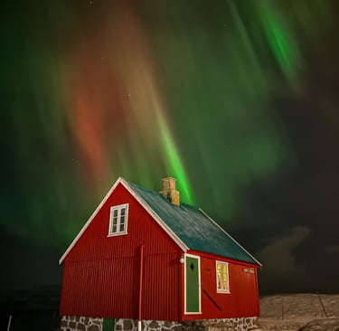 Red house under vivid green and red Northern Lights in snowy Faroe Islands landscape, winter aurora display.
