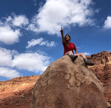 a woman sitting on a rock with her hand up to the sky