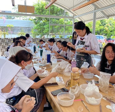 a large group of students sitting at a table making pottery
