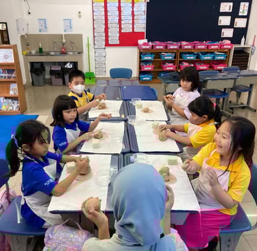 a group of children sitting at a table and making pottery together
