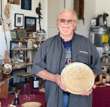 Woodturner Tom Baker holding his Big Leaf Maple Burl Platter, in front of show display