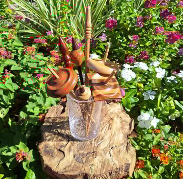 A sample of our spindle types. Seven assorted spindles in a glass vase in a garden of flowers.