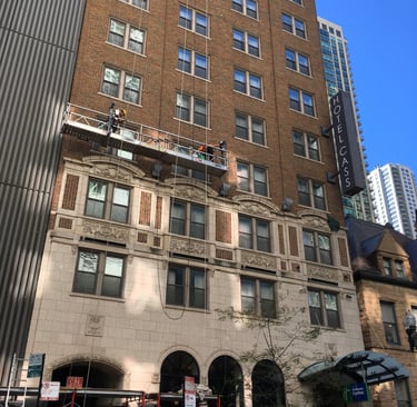 Masonry repair on the facade of a classic brick building using a suspended scaffold.