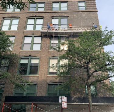 Masonry crew on scaffolding restoring the facade of a large brick apartment building.