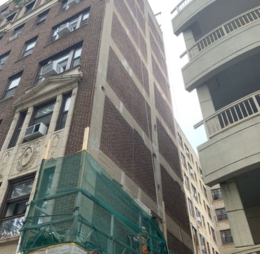 Facade repair on a brick and concrete building with scaffolding and green safety netting.