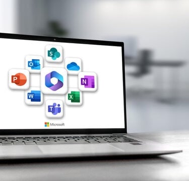 Laptop on desk displaying Microsoft 365 dashboard with Office app logos on screen.