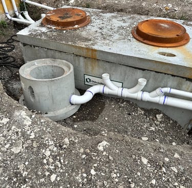 Underground concrete septic tank installation with PVC piping and riser access covers.