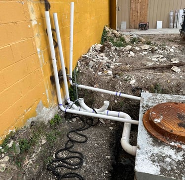 PVC plumbing pipes and a septic tank riser installed outside a yellow building wall.
