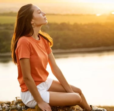 Mulher sentada ao ar livre, olhos fechados, respirando fundo e relaxando em um momento de tranquilid