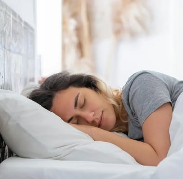 Mulher dormindo tranquilamente em cama com lençóis brancos, representando a importância do sono 