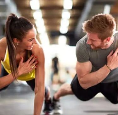 Mulher e um homem sorridente fazendo treino de força em academia