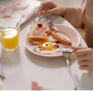 Uma mulher sentada a uma mesa com um prato de ovos, pão integral e suco de laranja 