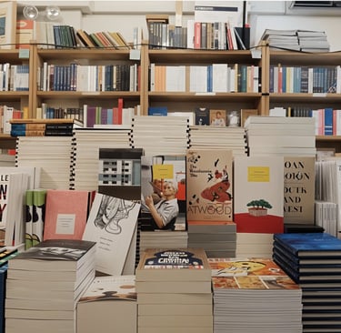 Books displayed on a table in front of shelves filled with various titles in a bookstore setting