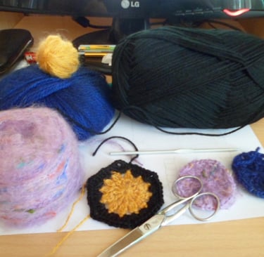 Pelotes de laines posées sur une feuille blanche qui est posé sur une table un crochet au milieu