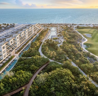 Aerial view of a luxury beachfront resort with a golf course and tropical gardens at sunset.