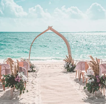 Elegant beach wedding ceremony setup with rose gold chairs and pampas grass decor overlooking the turquoise ocean.