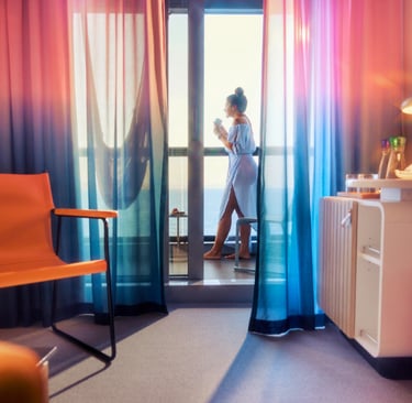 A traveler drinking coffee on a cruise ship balcony with colorful ombre curtains and modern cabin decor.