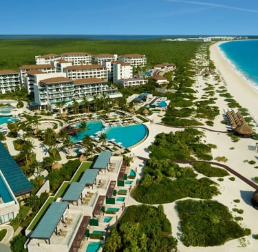 Aerial view of a luxury beachfront resort in Cancun with swimming pools, white sand, and turquoise ocean water.