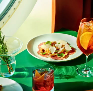 Italian beef carpaccio with parmesan cheese served alongside an Aperol Spritz cocktail on a green table.