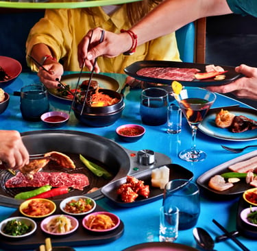 Friends dining at a Korean BBQ restaurant with wagyu beef grilling over an inset tabletop burner.