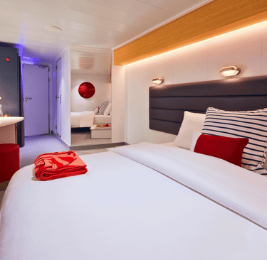 Modern cruise ship cabin featuring a plush bed with nautical striped pillows and a vanity desk.