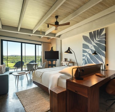 Modern luxury hotel suite with a wooden desk, king bed, and balcony overlooking a scenic landscape.