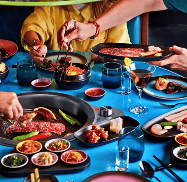 Friends dining at a Korean BBQ restaurant grilling Wagyu beef and enjoying traditional banchan side dishes.