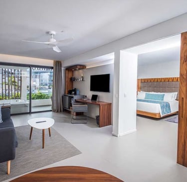 Modern hotel suite with a living area, work desk, and bedroom view through a sliding wooden door.