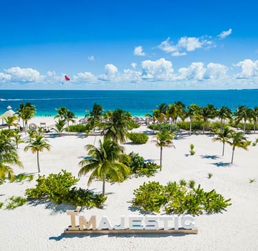 Aerial view of Majestic Resorts white sand beach with palm trees and turquoise Caribbean water.