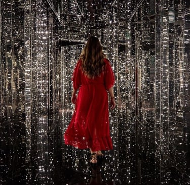 Woman in a flowing red dress walking through an immersive infinity mirror room with glowing fairy lights.